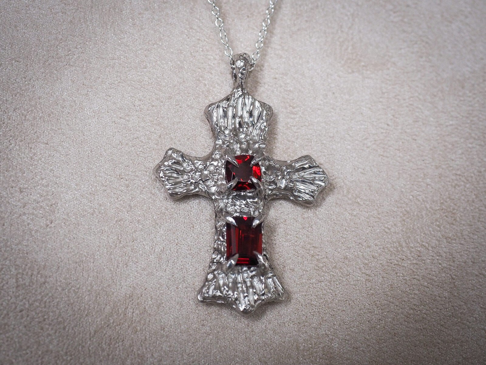 Close-up of the cross pendant, showing the hand-textured surface and claw-set garnets