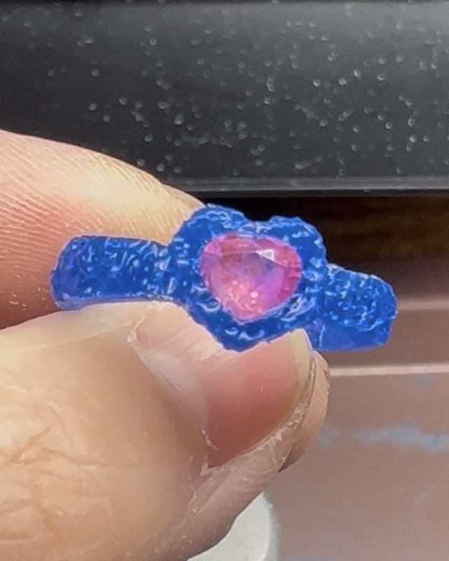 The initial wax design of Suzie’s ring in blue wax, held between finger and thumb, with the heart-shaped pink sapphire in its bezel