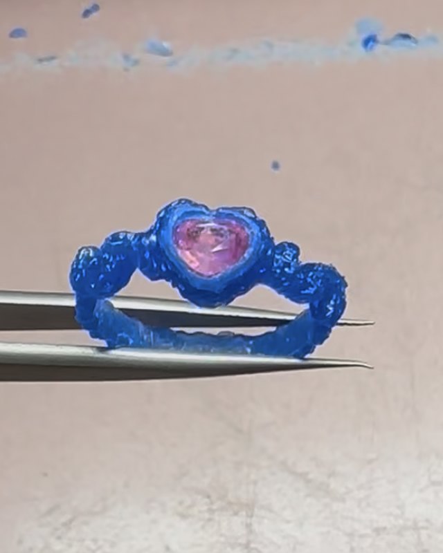 The final blue wax ring seen front on in tweezers, with the heart-shaped pink sapphire set in the bezel