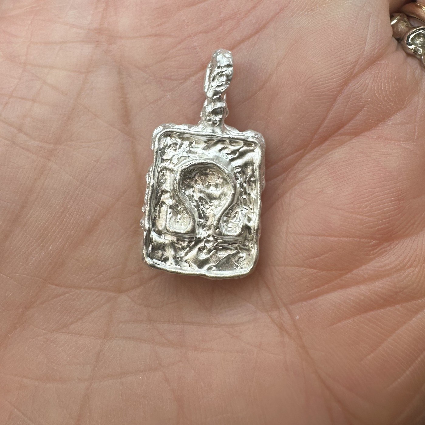 A raw silver pendant, freshly cast and not yet polished, shown in the palm of the hand