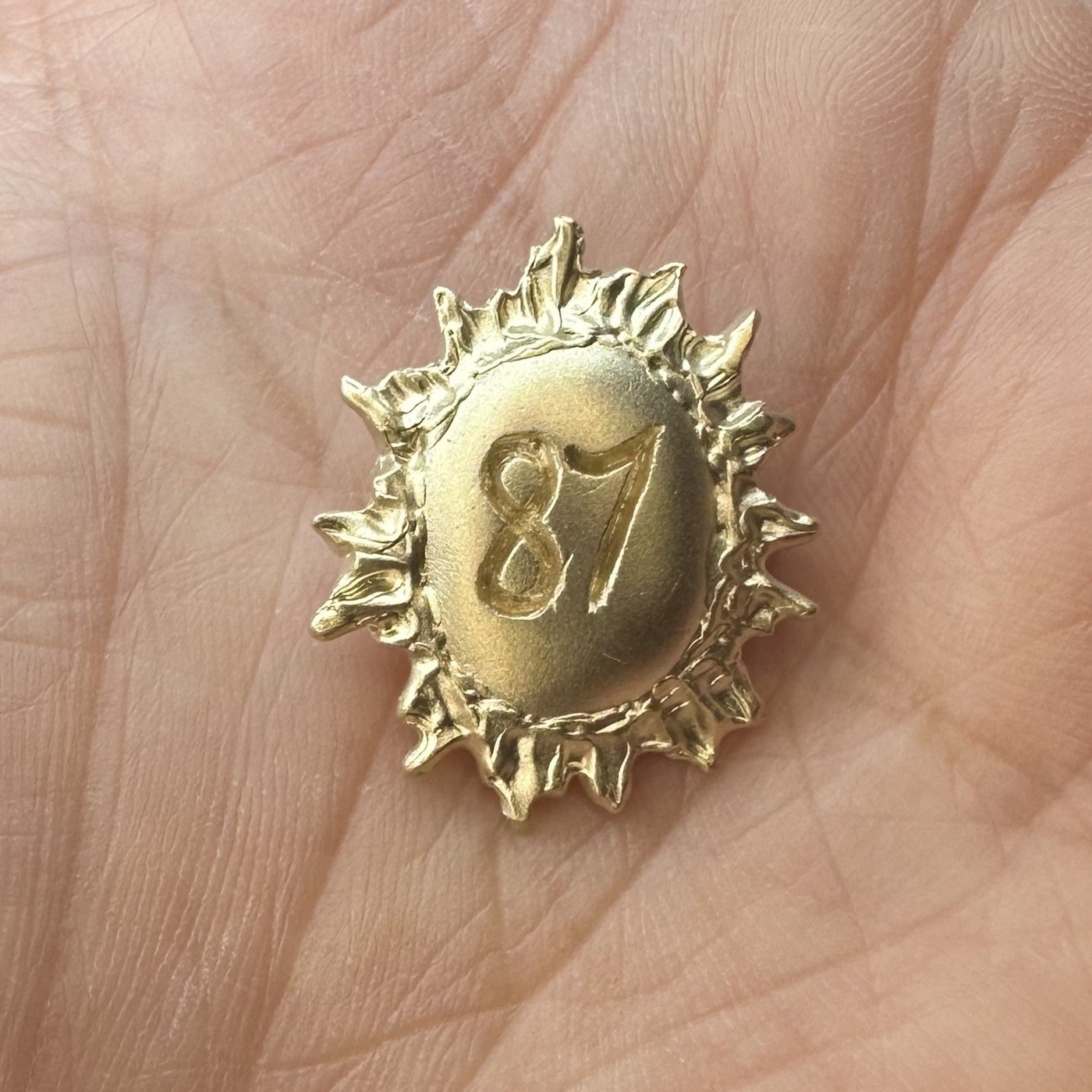A raw 9ct gold sunburst pendant, freshly cast and not yet polished, shown in the palm of the hand
